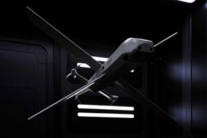 A futuristic HX-2 drone with a sleek, gray body and long wings, suspended in a dark, high-tech hangar with glowing lights.