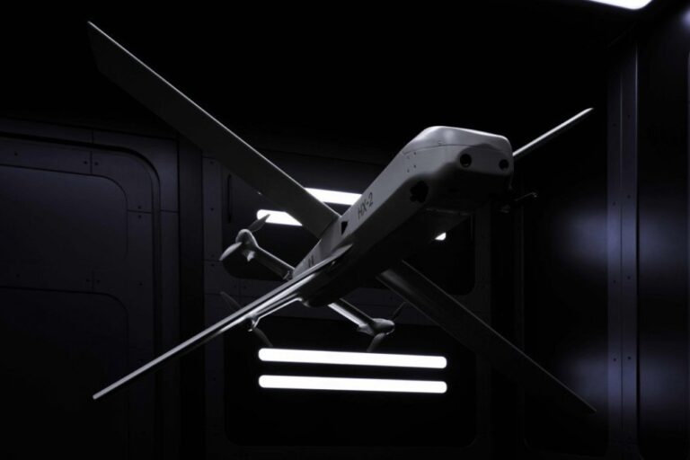 A futuristic HX-2 drone with a sleek, gray body and long wings, suspended in a dark, high-tech hangar with glowing lights.