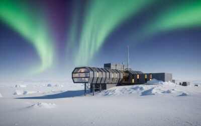 Dramatic image of a modern research station in Antarctica with snow-covered landscape, high-tech buildings on stilts, and vibrant aurora borealis in the night sky.