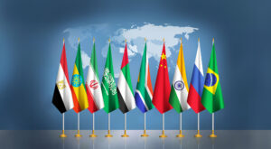 A row of flags from different countries standing on poles against a backdrop of a world map.