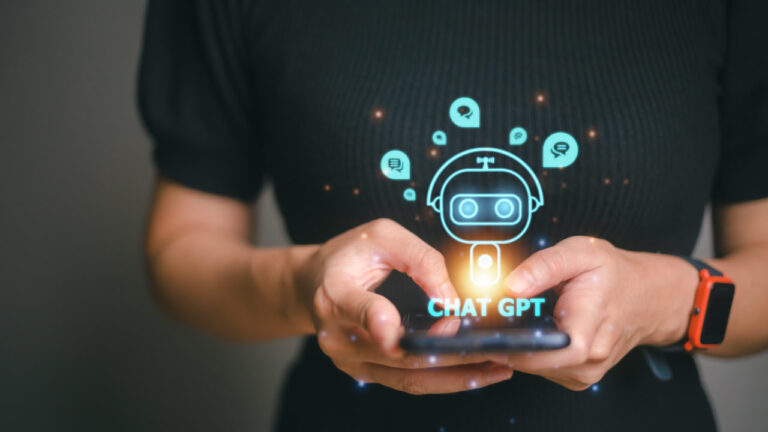 A person holding a smartphone with a holographic Chat GPT interface and robot icon, surrounded by speech bubbles, on a dark background.