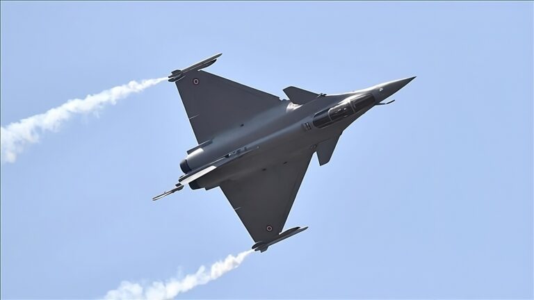A sleek French Rafale fighter jet flying upward against a clear blue sky, with white smoke trails streaming from its wings, highlighting its aerodynamic shape and military prowess.