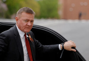 A blurred figure lies on the ground surrounded by emergency responders near a tall building, with the Kremlin’s silhouette faintly visible through a foggy sky, suggesting a mysterious urban incident.