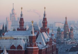 A stunning cityscape featuring the historic Moscow Kremlin with its ornate towers, domes, and fortress walls, set against a hazy winter morning sky.