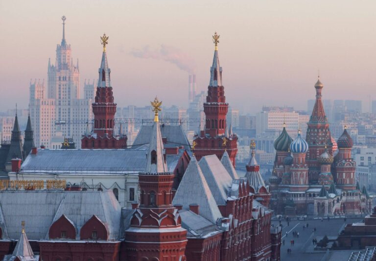 A stunning cityscape featuring the historic Moscow Kremlin with its ornate towers, domes, and fortress walls, set against a hazy winter morning sky.