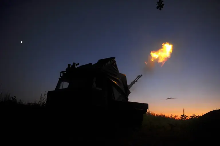 Silhouette of a military vehicle firing a bright muzzle flash against a twilight sky with a crescent moon and distant horizon.