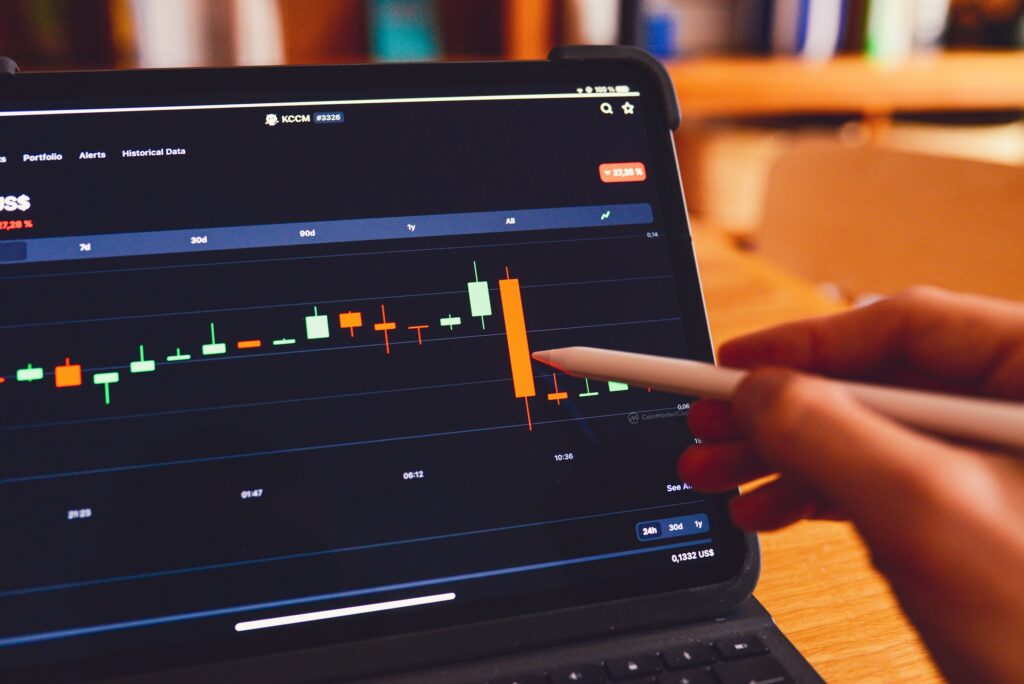 A hand using a stylus on a tablet displaying an interactive financial chart with candlestick patterns and market data.