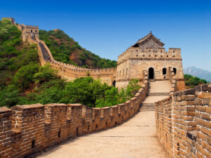 A scenic view of the Great Wall of China winding through green hills and mountains, with stone towers and pathways.