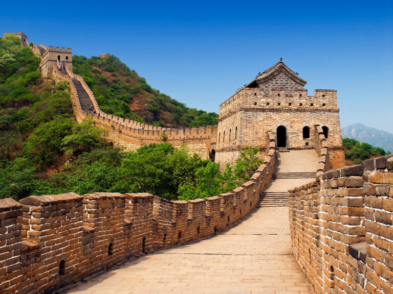 A scenic view of the Great Wall of China winding through green hills and mountains, with stone towers and pathways.