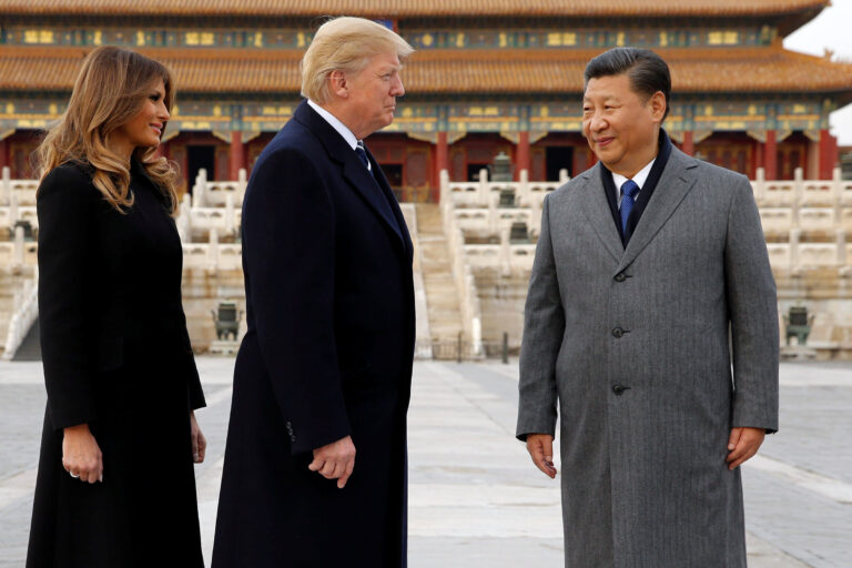 Donald Trump and Xi Jinping standing together in Beijing, with Melania Trump, in front of a traditional Chinese palace.