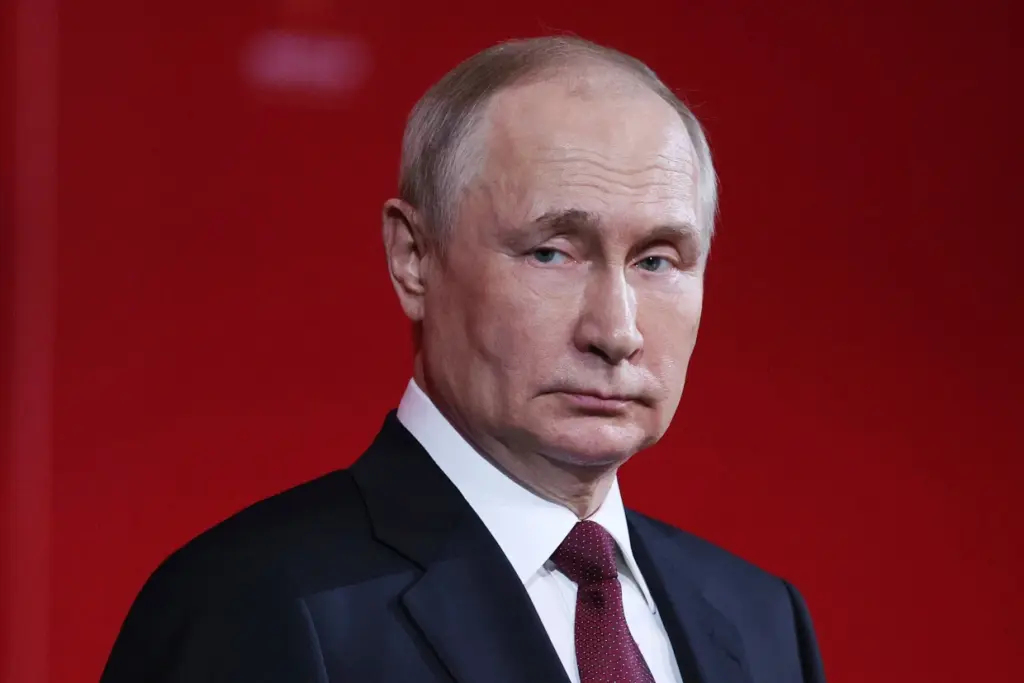 A portrait of Vladimir Putin, Russian President, dressed in a dark suit with a red tie, set against a solid red background, conveying a sense of authority and intensity.