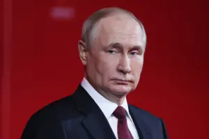 A portrait of Vladimir Putin, Russian President, dressed in a dark suit with a red tie, set against a solid red background, conveying a sense of authority and intensity.